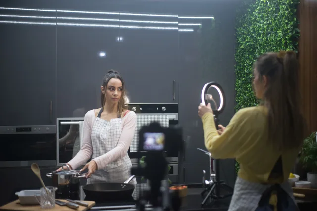 Two women creating a cooking video in a stylish kitchen setup with ring light. Creator collaborations for audience growth