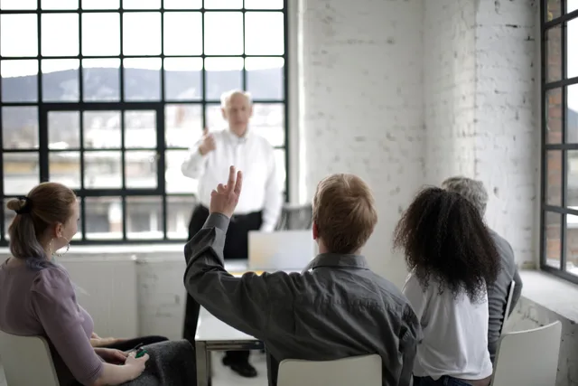 Group of adults in a discussion, with one person raising a hand in a bright office space. Finding content ideas from audience questions