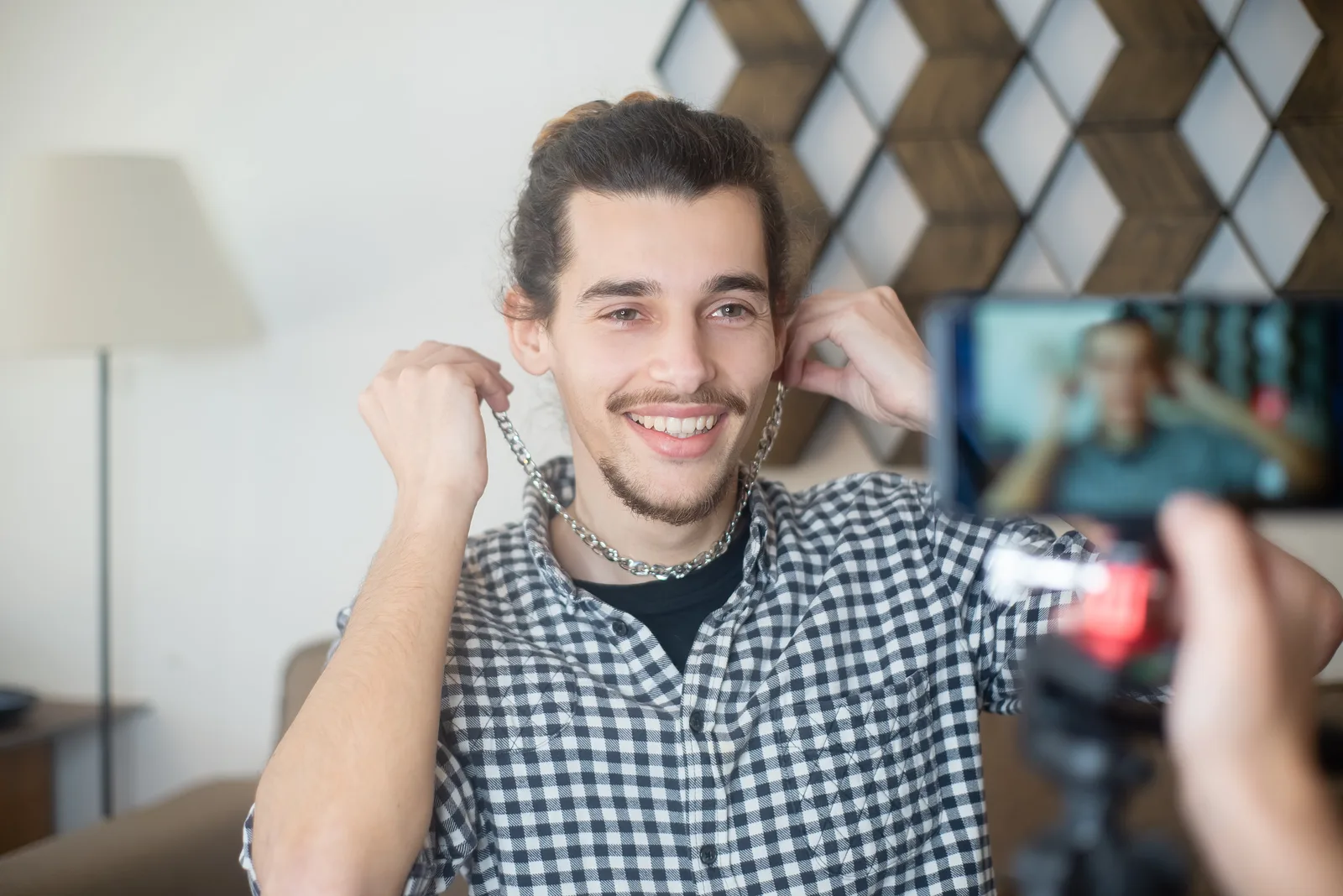 Smiling man vlogging indoors with a smartphone camera, creating online content.